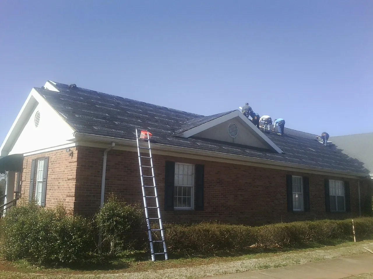 Crew tearing shingles off a brick ranch roof with a ladder set — Metal Roof Repair work by our crew in Mountville