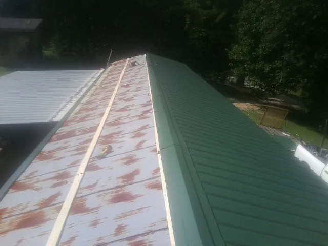 Old rusted panels beside newly installed green metal roofing in Mountville