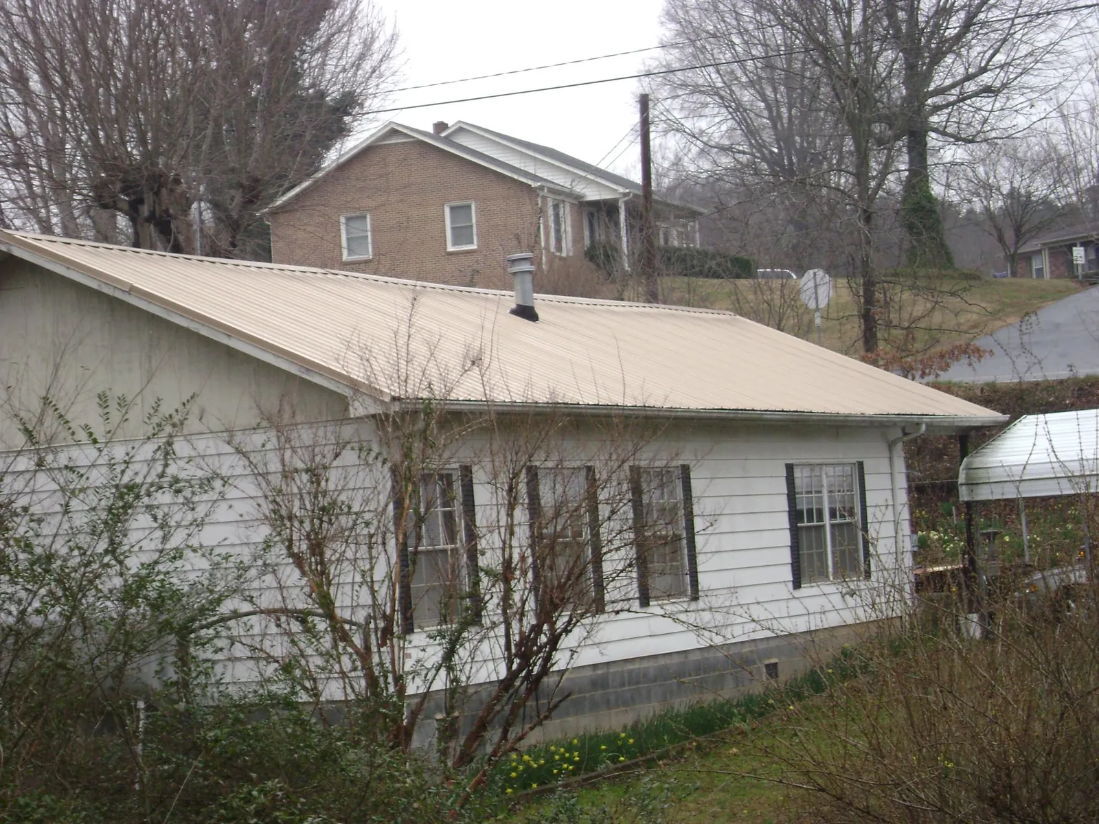 Tan metal roof on a white sided house set into a hillside — Commercial Roofing by Roofing Brothers in Mountville
